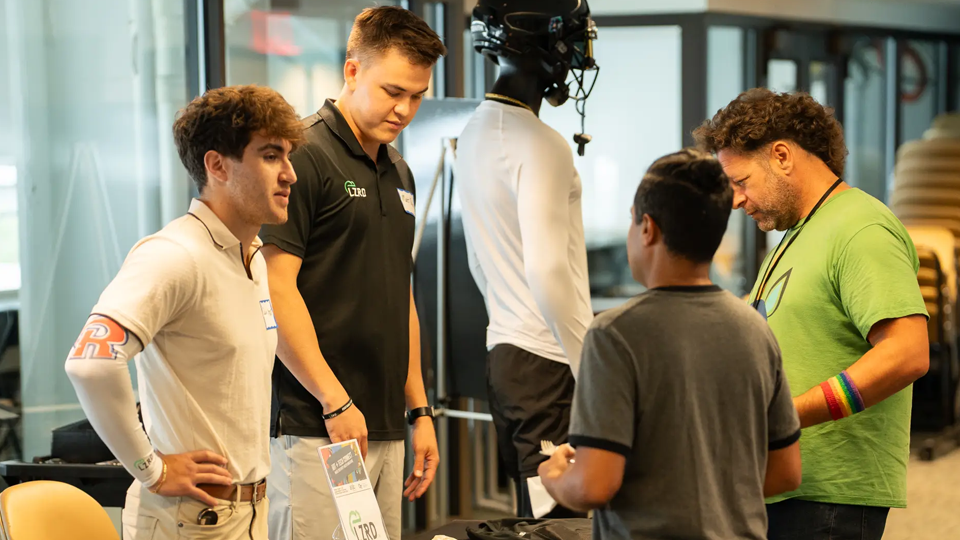 three students behind a table talking to two other students