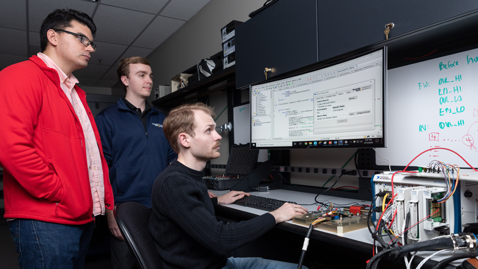 three researchers staring a large computer monitors results