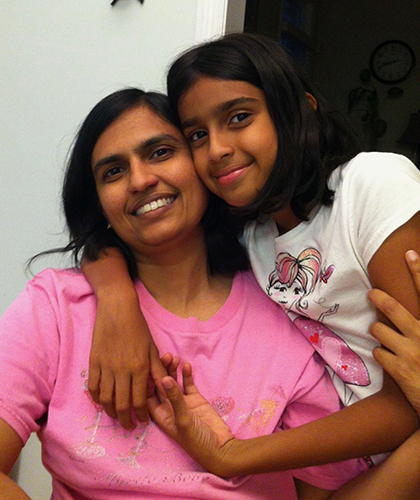 Mother and daughter smiling and embracing while posing for a photo indoors.
