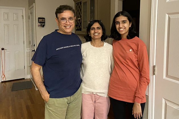 Father, mother, and daughter standing together indoors and smiling at the camera.