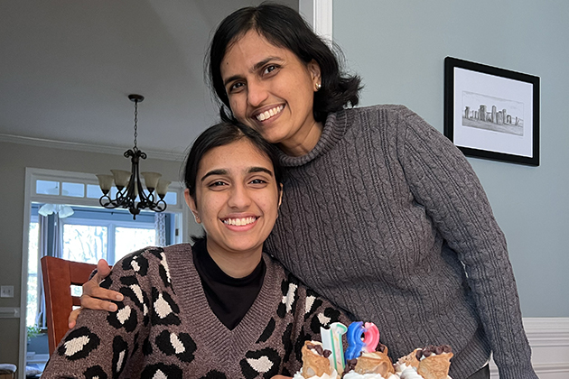 Mother and daughter smiling together while celebrating a birthday with a cake and lit number candles.