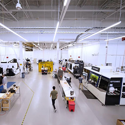Wide view of a manufacturing lab with industrial machines, workstations, and a person walking down a central aisle.