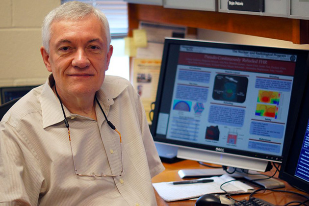 Person seated at a desk in an office environment with a computer monitor displaying a detailed research poster.