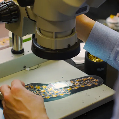 Close-up of a researcher examining a flexible electronic device under a microscope.