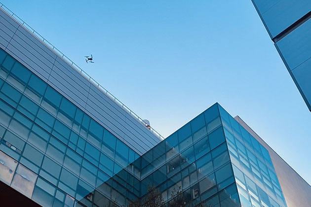 A drone flying high between several buildings with the sky in balckground.