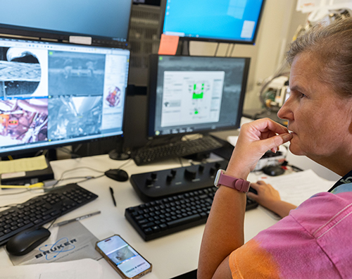 Person seated at a workstation viewing scientific images and data on multiple computer monitors.