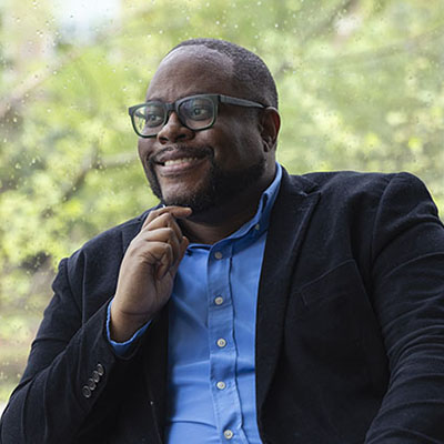 Person wearing glasses and a blue shirt seated indoors near a window.