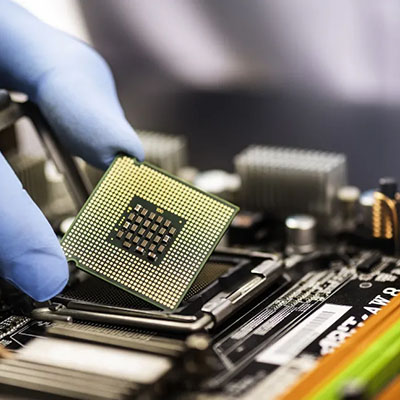 Gloved hand holding a computer processor above a circuit board.