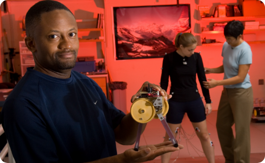 researcher holding device in hands. Behind him are another researcher and patient standing.