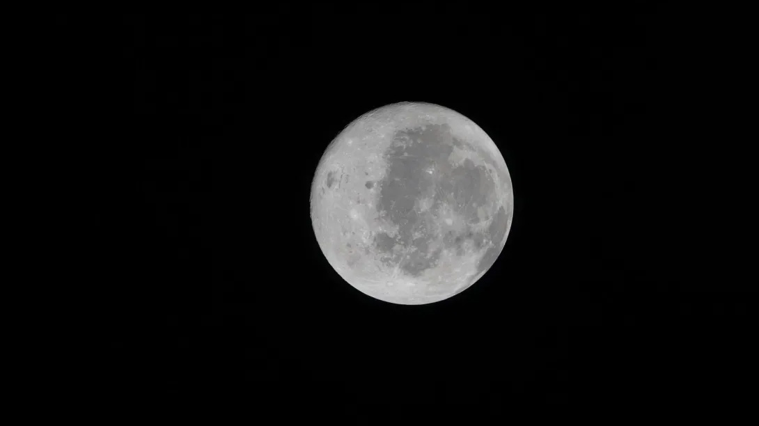 The full moon appears against a black night sky, with surface features and craters visible in detail.