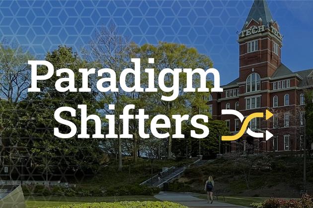 Promotional graphic for the "Paradigm Shifters" series featuring large white text over a campus scene with a red-brick academic building, trees, a walkway, and a blue hexagonal overlay pattern. A yellow-and-white directional arrow logo appears beside the title.