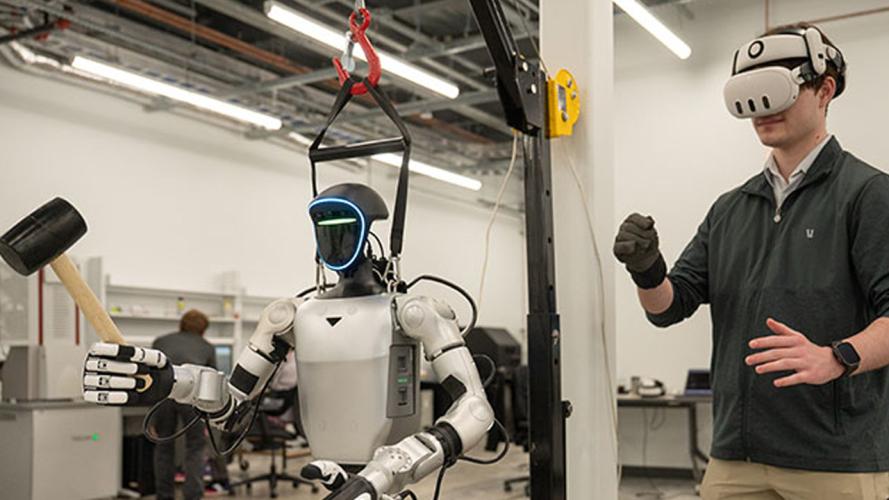 Person wearing a virtual reality headset controlling a humanoid robot equipped with tools in a laboratory setting.