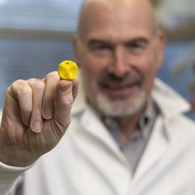 male researcher in a white lab coat holding a yellow 3D printed heart valve