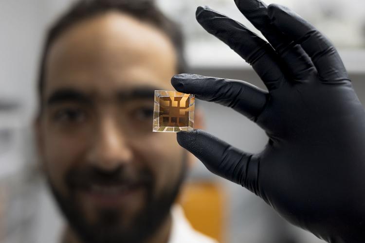 A male Georgia Tech researcher wearing a black glove holds a solar cell prototype.