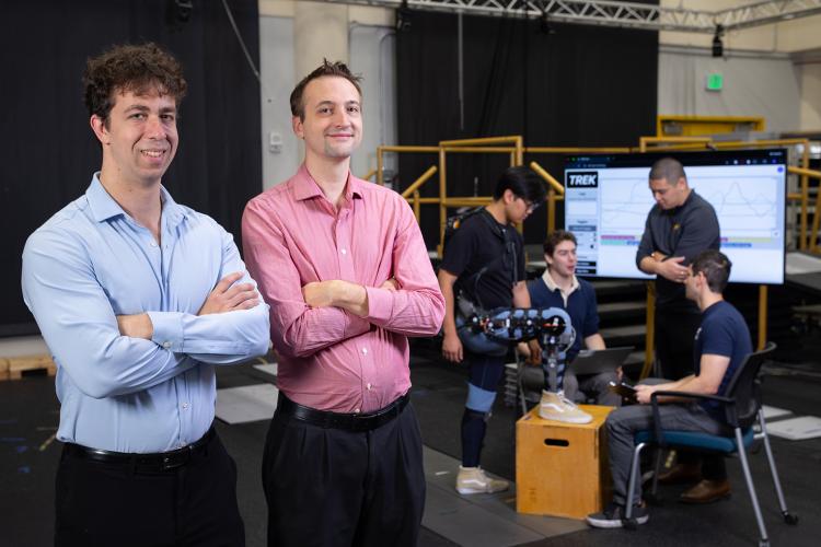 Matthew Gombolay and Aaron Young pose in the lab while Ph.D. researchers work on a leg exoskeleton device.
