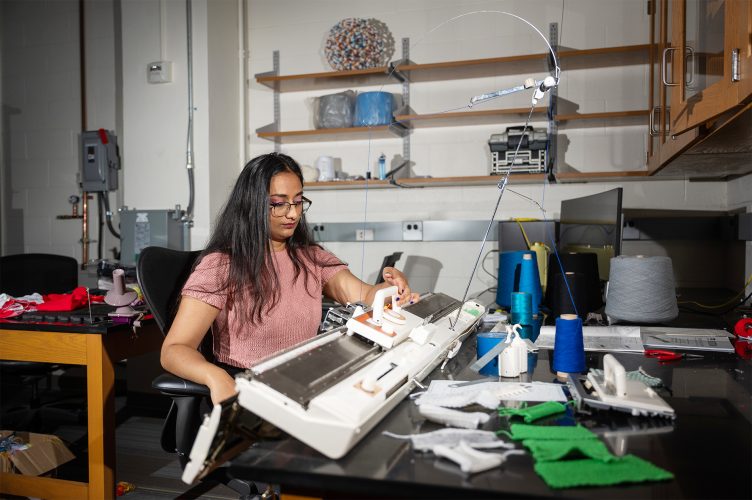 A female student operating a knitting machine in a research lab at Georgia Tech.