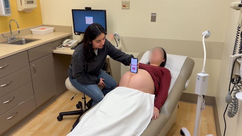 Woman holds mobile phone to the belly of a pregnant woman