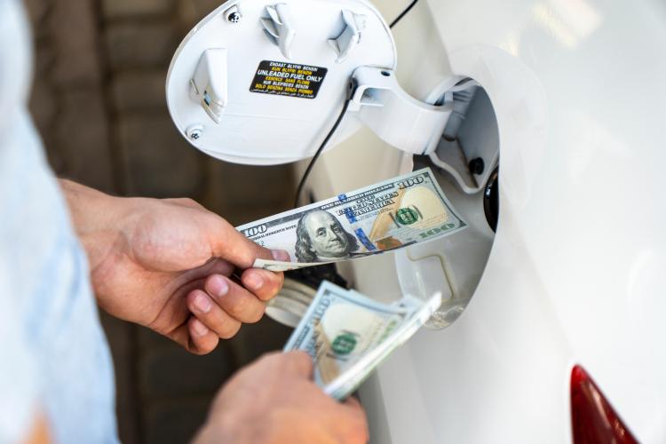 Hand of the man putting money into the opening gas tank of his car. Refueling car with gasoline at gas stations. 