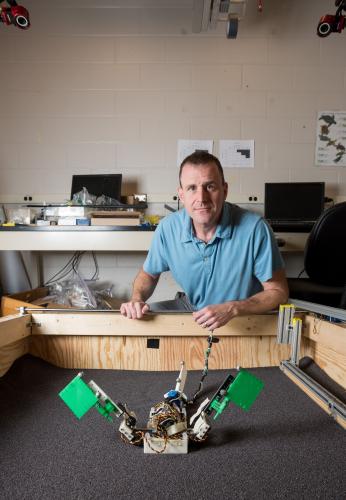 Man in a blue shirt posing behind a robot.