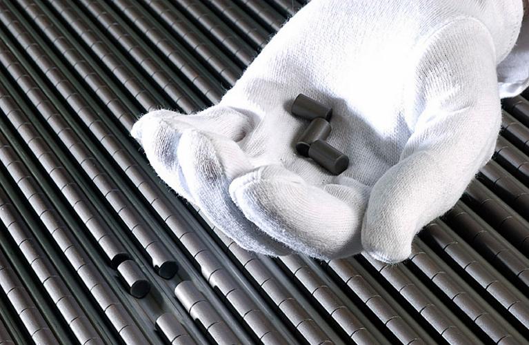A white gloved hand holds 3 nuclear pellets with rows of nuclear pellets in the background