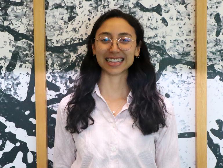 A smiling woman standing in front of a wall. The wall has a unique pattern and wood frames.