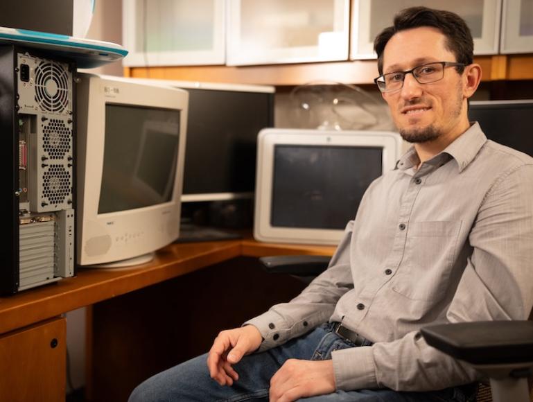 Zsolt Kira sitting in office chair surrounded by old computers