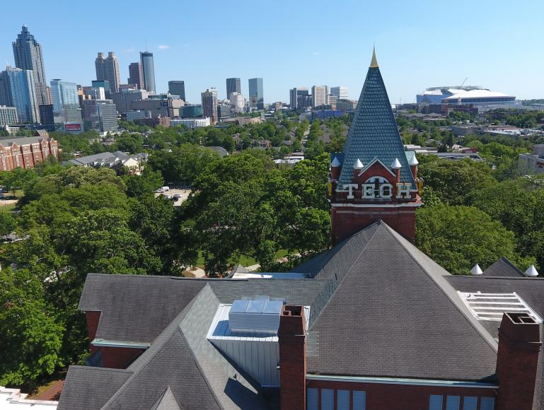 Aerial view of Georgia Tech’s historic campus in Atlanta, with the Tech Tower prominently in the foreground and the Atlanta skyline visible in the background under a clear blue sky.