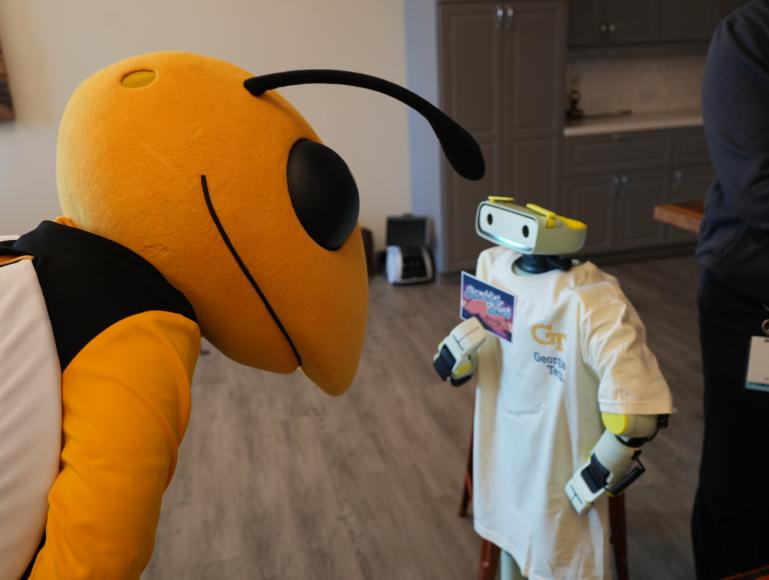 Photo of Buzz the mascot leaning down toward a small humanoid robot wearing a Georgia Tech t-shirt