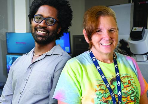 Two people together in a laboratory with computer monitors and scientific equipment in the background.