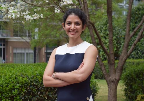 Farzaneh Najafi standing outside smiling with her arms crossed. Green foliage is visible in the background.