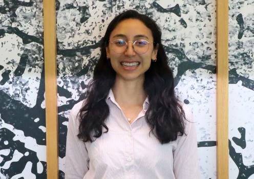 A smiling woman standing in front of a wall. The wall has a unique pattern and wood frames.
