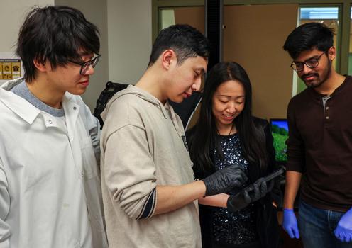 Associate Professor Yuhang Hu and three male students from her lab gather around and look at a soft adhesive hydrogel they are studying.