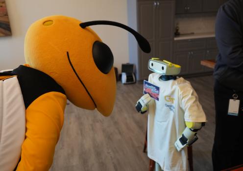 Photo of Buzz the mascot leaning down toward a small humanoid robot wearing a Georgia Tech t-shirt