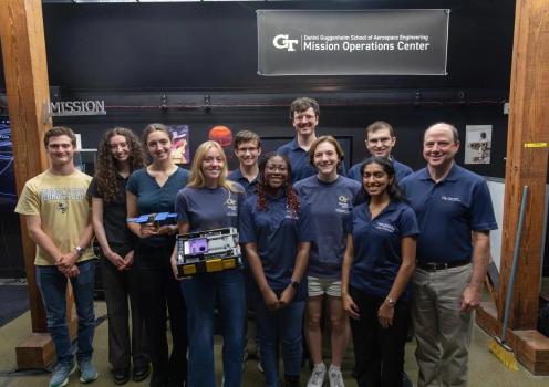 Georgia Tech students, faculty, and staff pose with spacecraft hardware beneath the Daniel Guggenheim School of Aerospace Engineering Mission Operations Center sign.