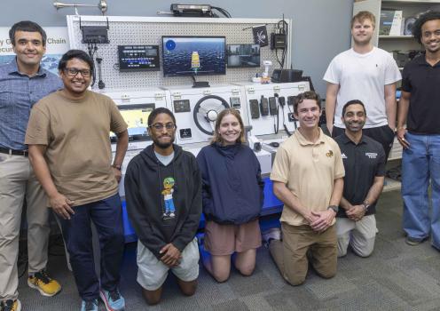 A group photo of students and faculty standing around lab equipment found on a ship. 