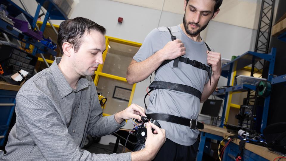 Researcher Aaron Young makes adjustments to an experimental exoskeleton worn by then-Ph.D. student Dean Molinaro.