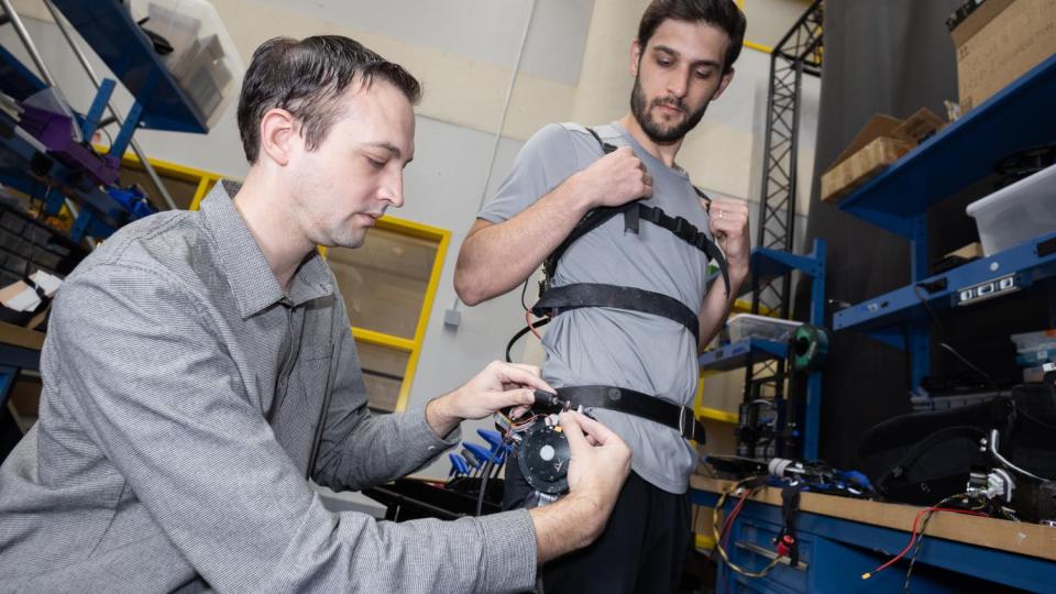 two people in the lab make adjustments to a robotic exoskeleton