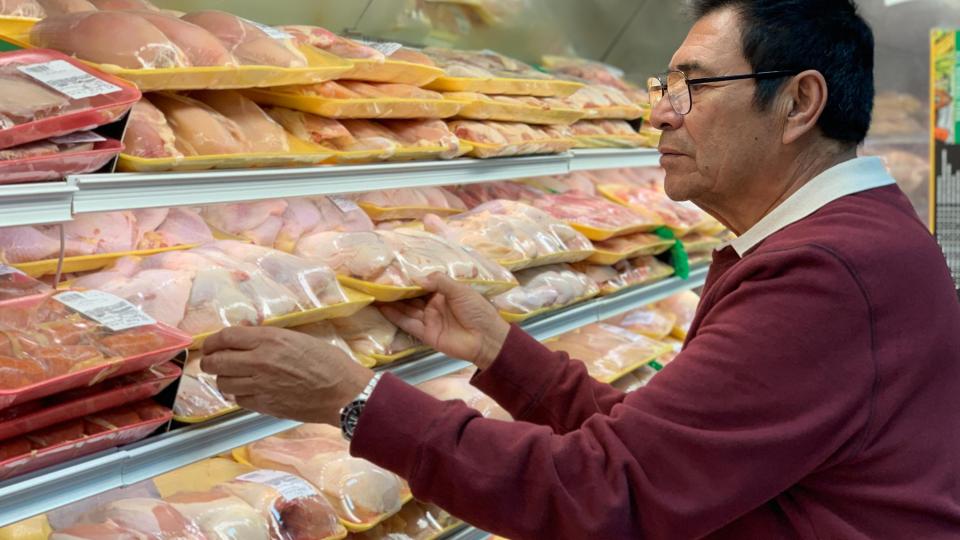 A man in a crimson colored sweater peruses the meat cooler in a supermarket.