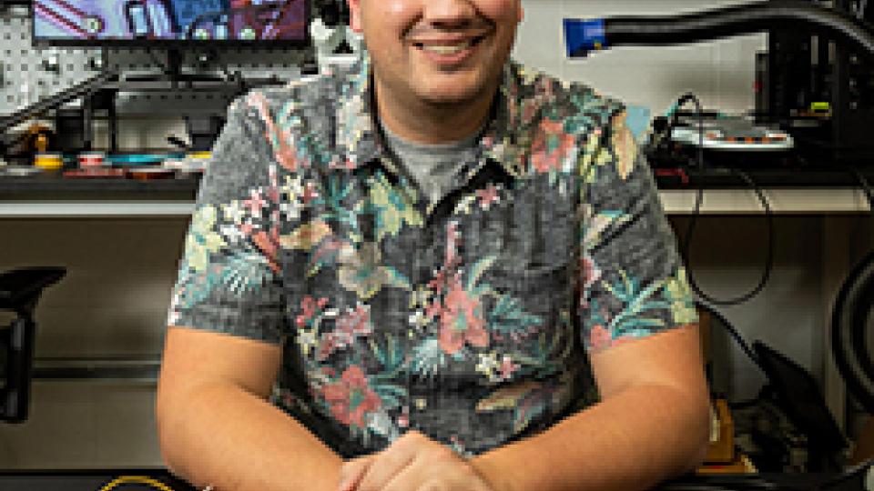 Josiah Hester sits at a desk in an electronics lab at Georgia Tech with an array of prototype projects and test equipment in front of him.