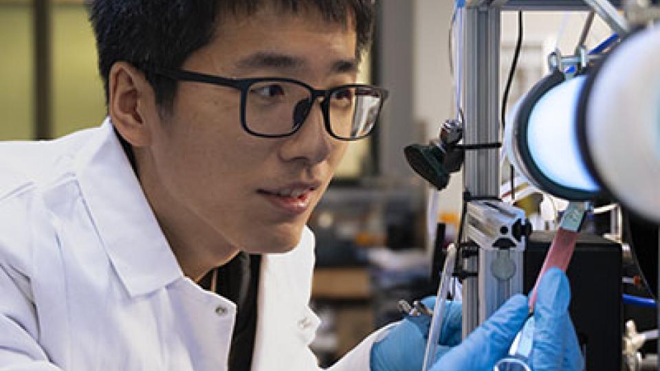 researcher with a white coat looking into a microscope