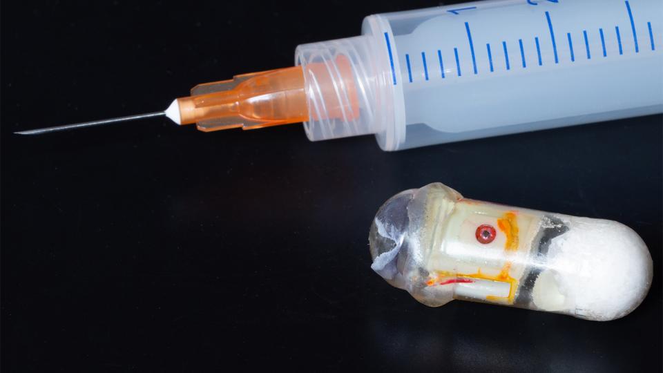 Prototype of an "exploding" capsule next to a syringe. The capsule can deliver medications that are typically only effective if injected.