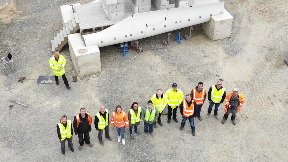 Overhead view of the Re-Wind crew doing structural testing on a decommissioned wind turbine blade bridge on an industrial lot.