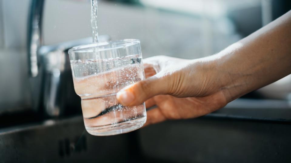Hand holds glass over faucet