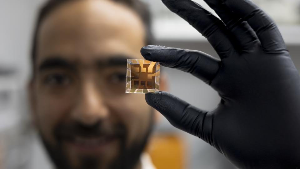 male researcher wearing a black glove holds a solar cell prototype