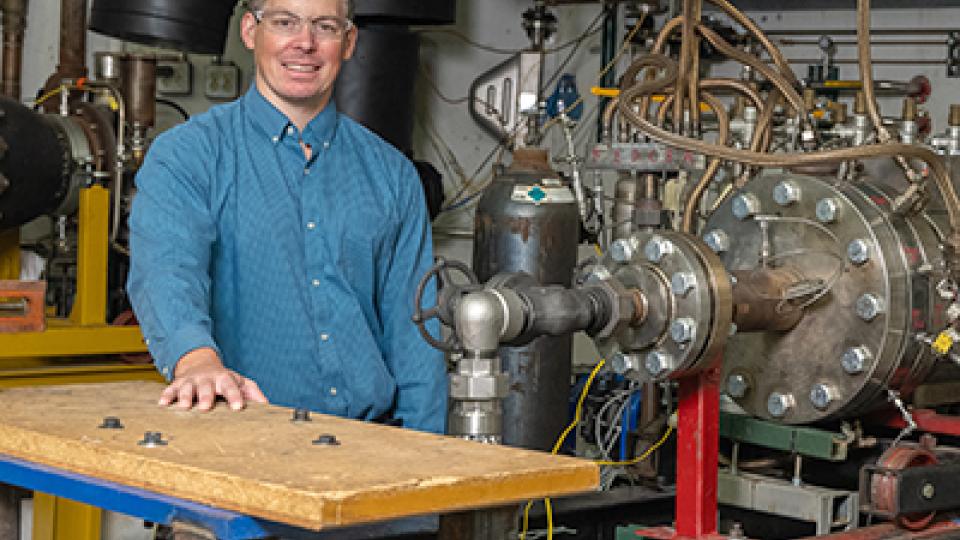 Benjamin Emerson stands with the high pressure liquid sprays combustor rig that his team uses to test novel combustor concepts.