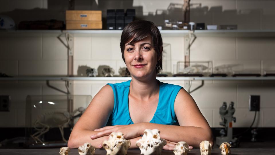A woman stands behind a row of skulls.