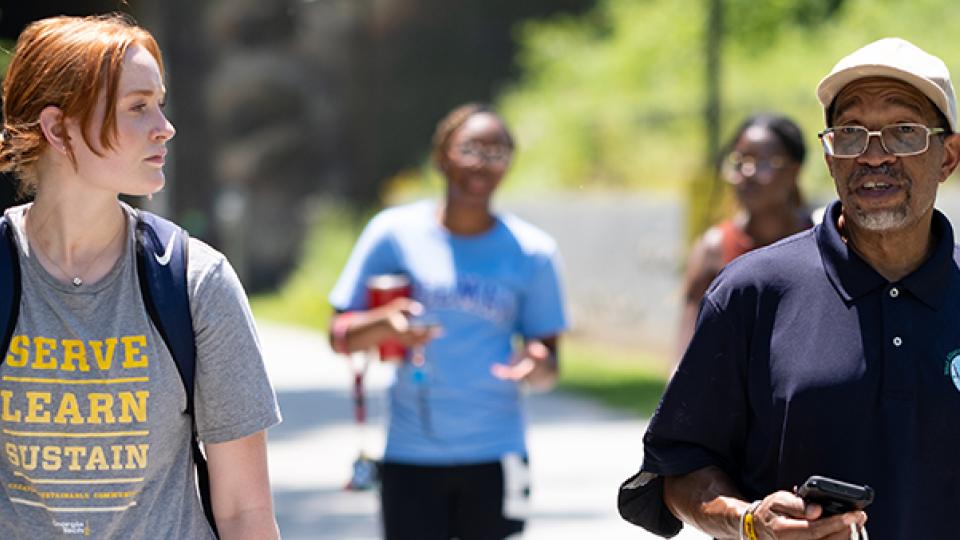 Photo Credit Ben Gray, AJC. A student wearing a "Serve-Learn-Sustain" tee shirt walks along a campus walkway with a Georgia Tech faculty member.