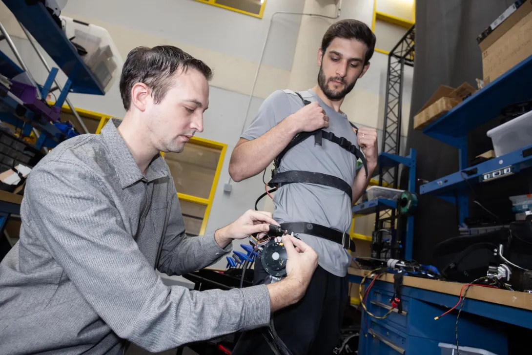 two people in the lab make adjustments to a robotic exoskeleton