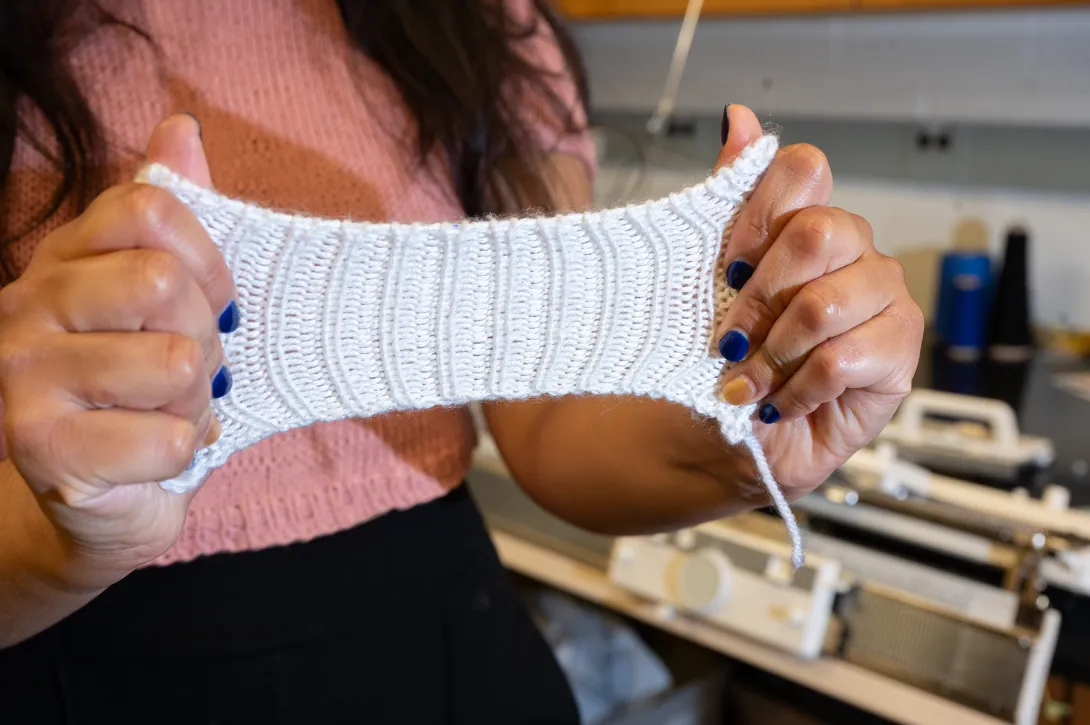 Hands stretching a small piece of white knit fabric to show its elasticity