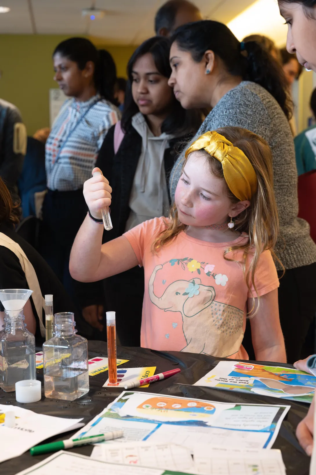 <div>This guest at Science and Engineering Day examines tiny living organisms in a test tube. (Credit: Joya Chapman)</div> Little girl in yellow headband examines a test tube.